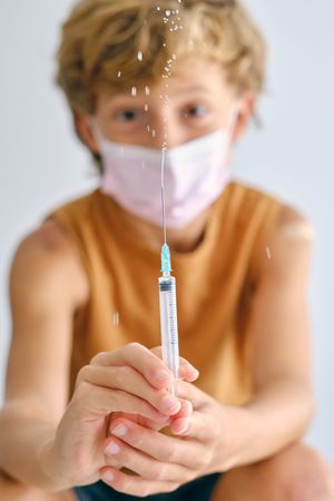 Boy in sterile mask sprinkling liquid medicament from syringe