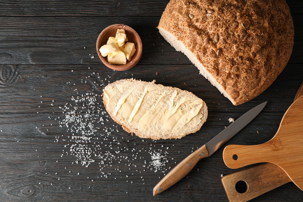Cutting boards, bread, salt, knife and butter on wooden background, top view and space for text