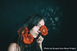 Studio portrait of mature woman with blue eyes holding gerbera flowers 56ElP0