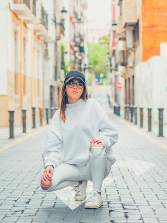 Young trendy woman sitting against street