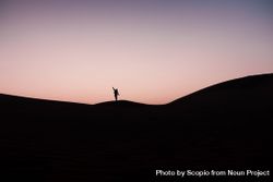Silhouette of person standing and raising an arm on hill during sunset 5k8y64