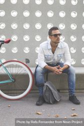Male sitting with bike parked in front of patterned cement wall, vertical 4j2394