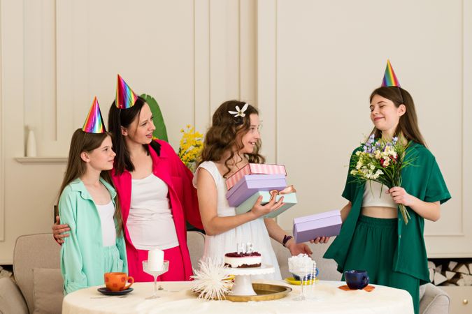 Girl holds gifts and flowers while family wearing festive hats