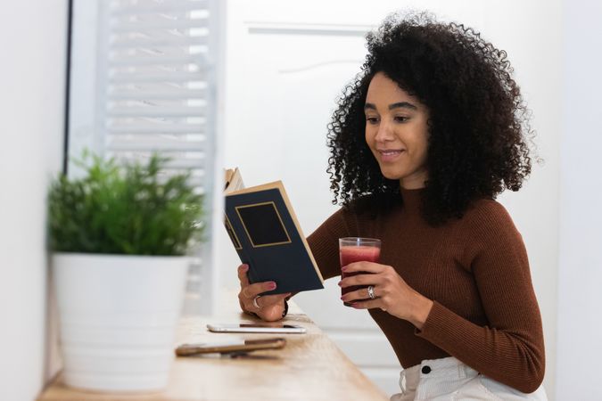 Black woman drinking smoothie and reading book in bar