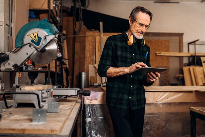 Older man with design plans on tablet in his woodwork shop
