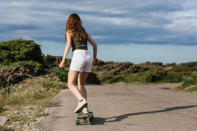 Anonymous woman riding longboard on asphalt road