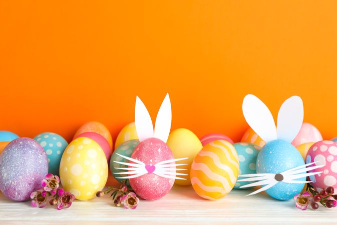 Decorated Easter eggs and cute bunny's ears on table against color background. Space for text