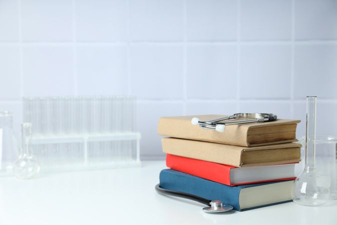Books, stethoscope and flasks on light background, space for text
