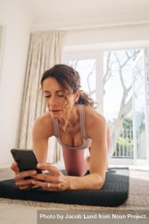 Woman using her smart phone to find workout tutorials online with exercising at home 5Qndm4