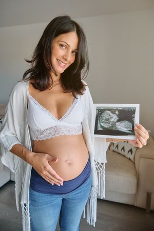 Smiling pregnant woman holding sonogram in living room