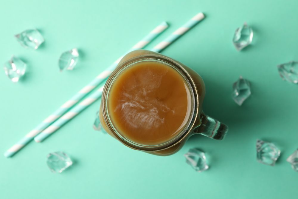 Jar of ice coffee, ice cubes and straws on mint background