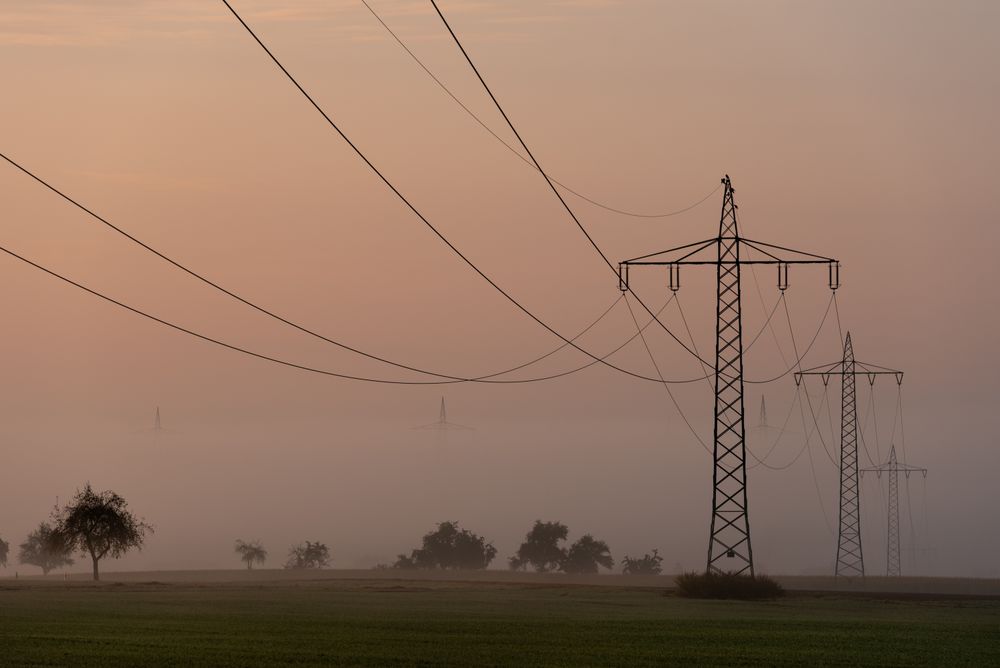 Electricity towers distribution through fog at sunrise, in a german village