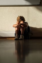 Upset boy embracing knees of floor in classroom