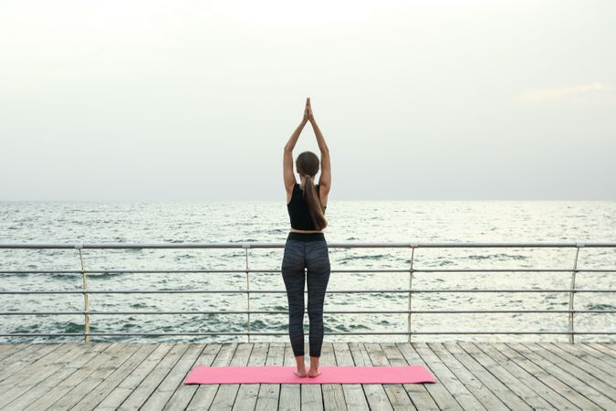 Woman on yoga mat on wooden floor at sea