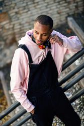 Male in overalls and pink hoodie leaning on railing of stairs outside