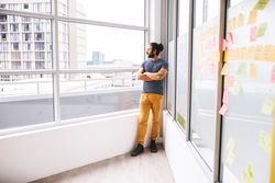 Young man staring out a window with a pensive look in office