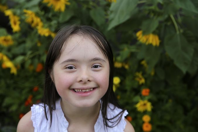 Adorable little girl smiling an d looking at camera with yellow flowers behind