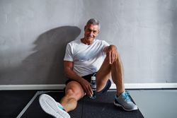 Man smiling and resting against wall with water after exercising