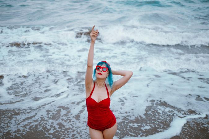 Cheerful stylish woman raising hands in foamy ocean water