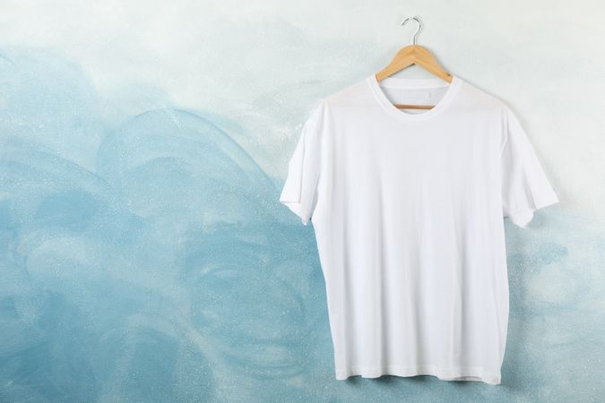 Hanger with blank t-shirt on blue background, space for text