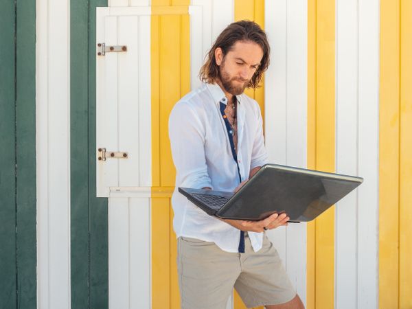 Cheerful guy using laptop near striped wall