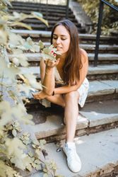 stylish woman sitting on stairs of park in New York smelling flowers