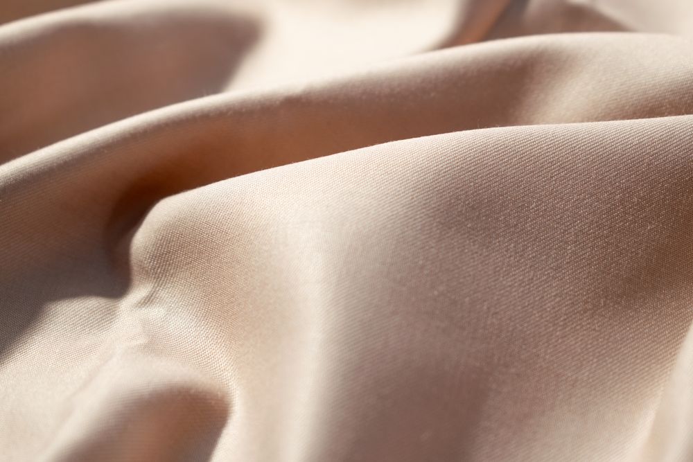 Close up silk shiny light brown fabric background texture.