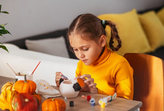 A little girl paints a clay hand made pumpkin. Halloween party. Crafts for children.