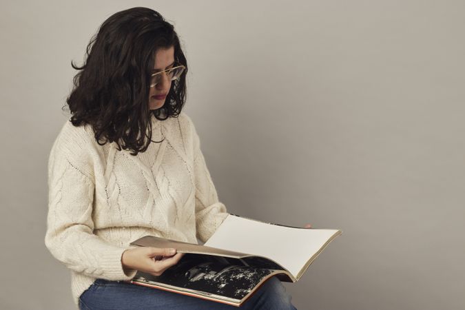 Focused young female looking through book in studio