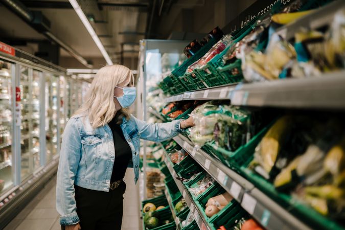 Grey haired woman reaching for vegetables in the produce aisle