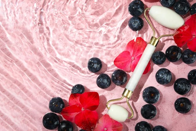 Top view of blueberries and flowers soaking in water with face roller with copy space