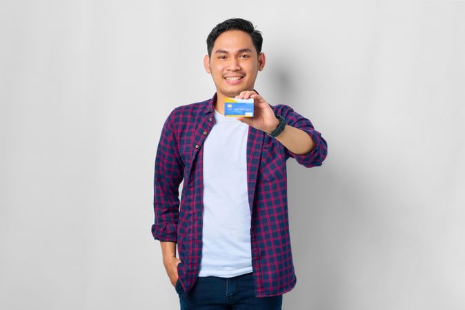 Asian male in grey studio holding up credit card