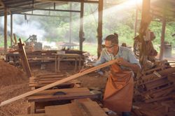 Carpenter cutting a piece of wood with the machine