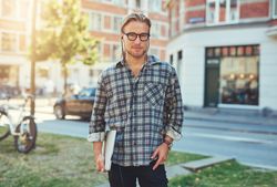 Man in glasses holding his laptop under his arm in a city park