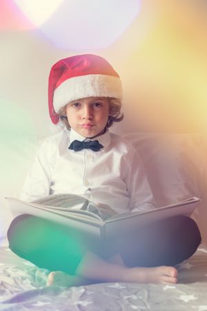 Bored boy in Santa hat reading book