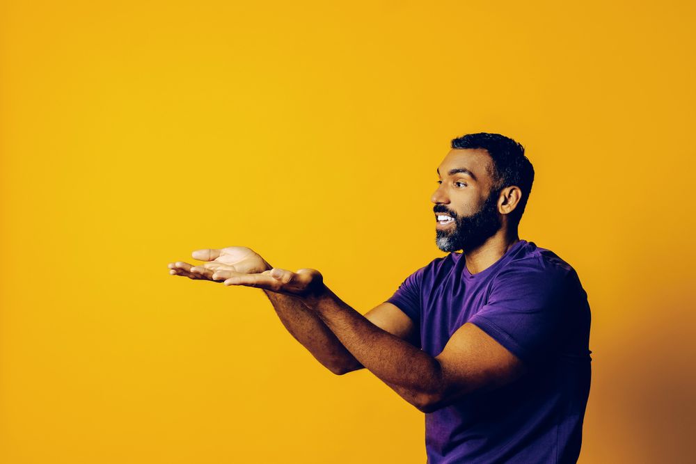 Black man in yellow studio with hands up to the copy space