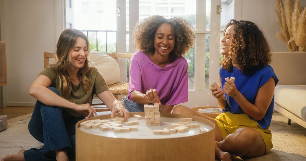 Group of Young Female Friends Playing a Physical Skill Blocks Game at Home in Cozy Sunny Living Room.