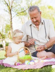 Grandfather and Granddaughter Coloring Easter Eggs on Blanket At Park