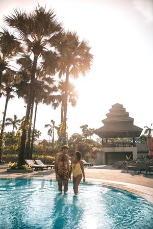 Man and woman standing in swimming pool near palm tree