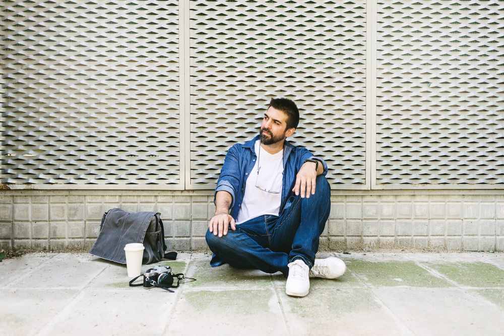 Latino man in denim relaxing on pavement outside with cup of coffee