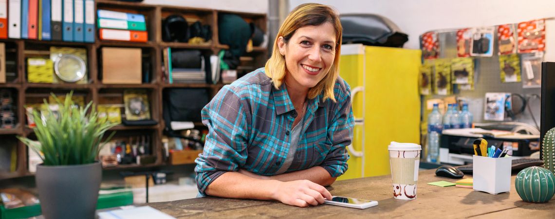 Banner of happy blonde woman entrepreneur looking at camera in local motorbike shop.