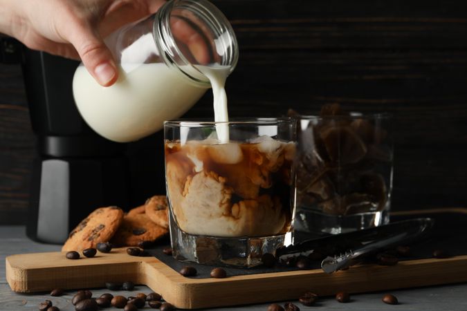 Woman pours a milk in glass of coffee. Composition with ice coffee