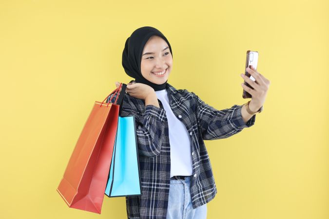 Cheerful Beautiful Asian Woman in Blue Shirt and Hijab Holding Shopping Bags