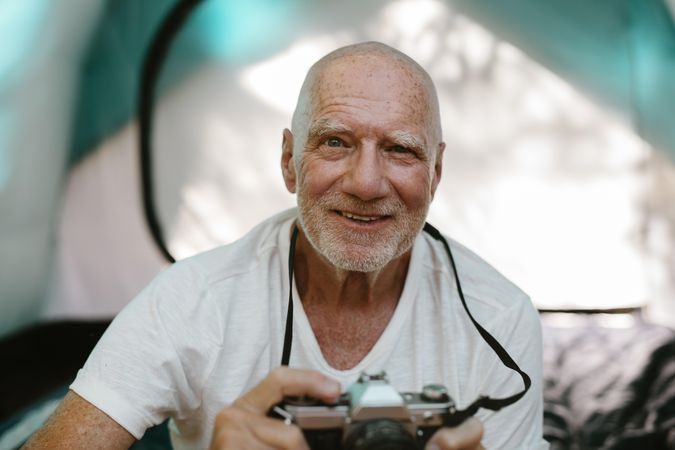 Closeup of a older man sitting outside his camping tent with a digital camera