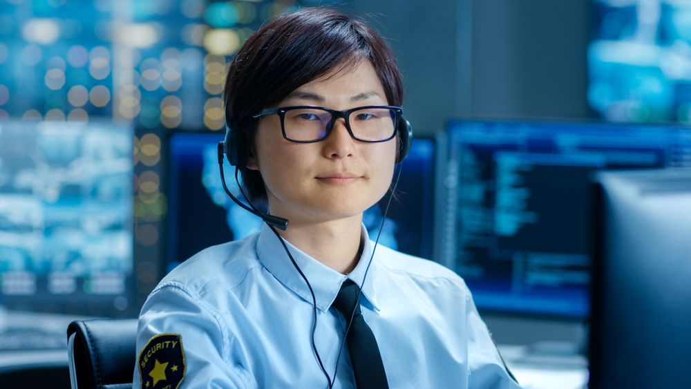In the Network Operations Center Senior Trader Teaches Young Associate to Makes Personal Client Call with a Headset.