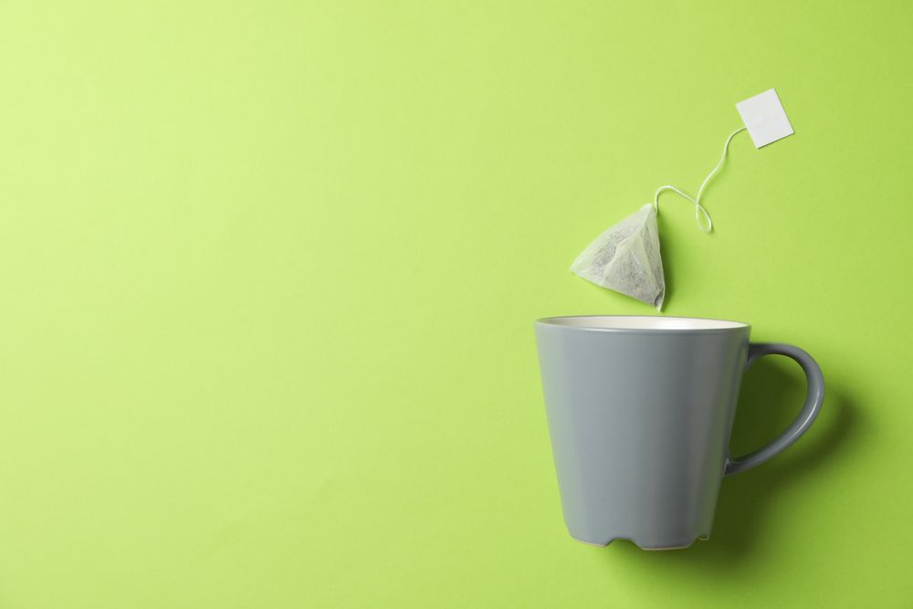 Cup and tea bag on green background, copy space