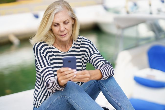 Older woman using her smartphone sitting on the dock