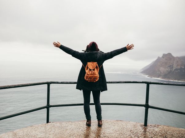 Female tourist with her arms outstretched looking at ocean