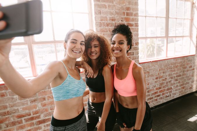 Group of happy young friends taking selfie with smartphone in gym