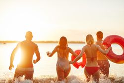 Multi-ethnic group of people running into the lake with floating rings